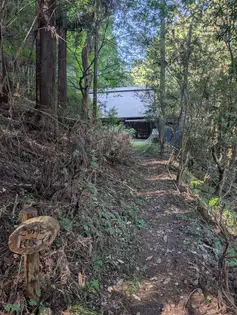 林の中の遊歩道。下に掲示板、右側に建物がある。