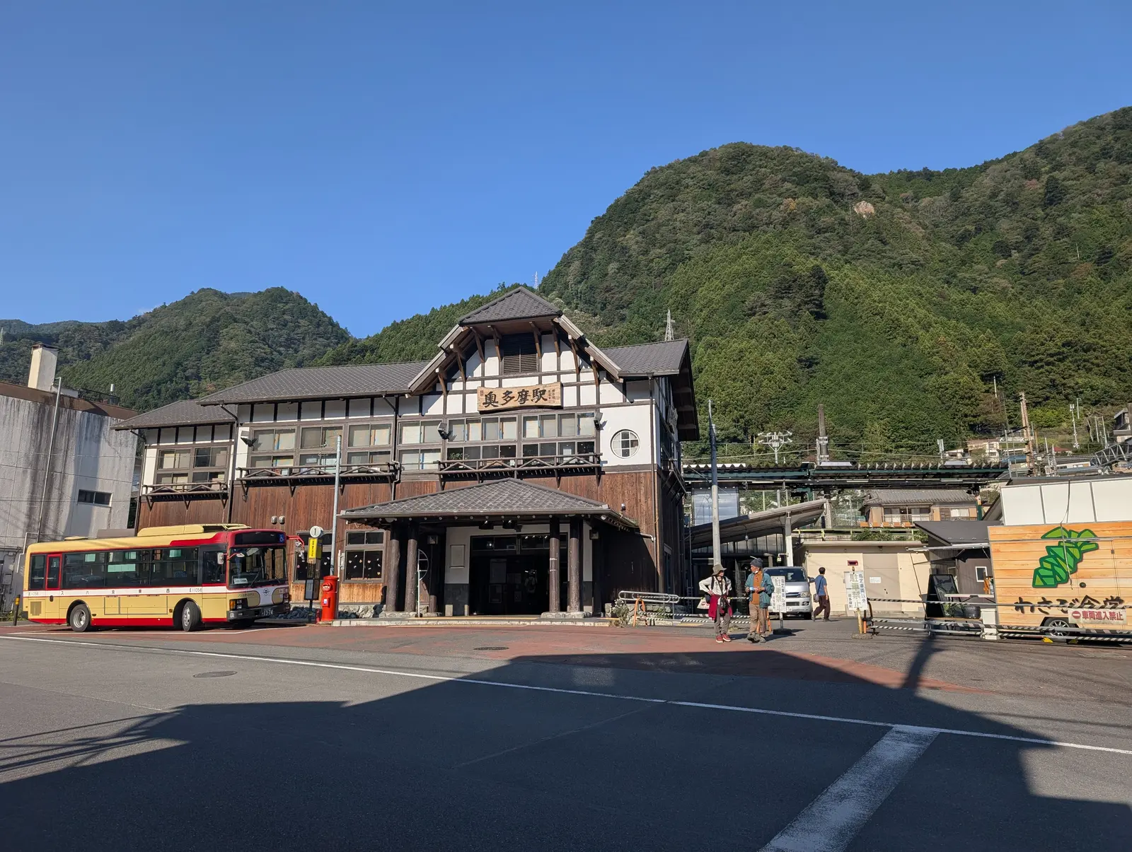 山のふもとのローカル駅。木造の駅舎と、駅前のバスと郵便ポスト。